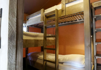 Habitación acogedora en una cabaña con literas de madera, almohadas blancas y paredes color naranja.