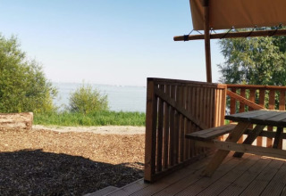 Scenic view from a lodge porch featuring a wooden picnic table, overlooking a lake with greenery.