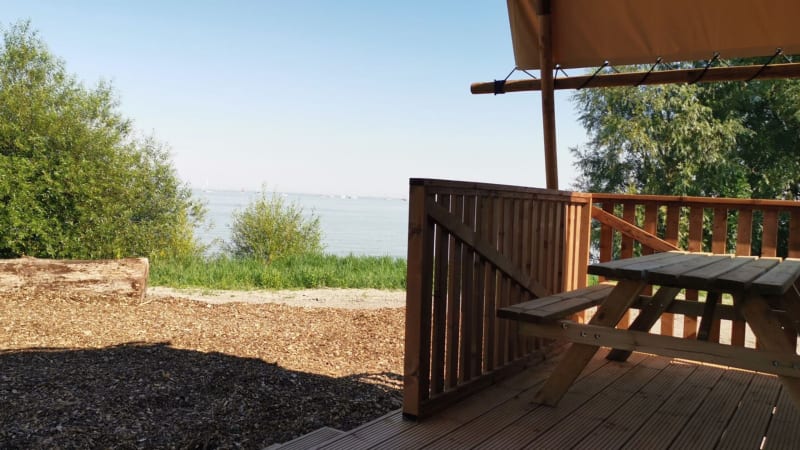 Vista desde la terraza de una cabaña con mesa de madera, mirando hacia el lago y vegetación verde.