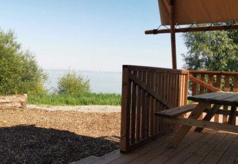 Vista desde la terraza de una cabaña con mesa de madera, mirando hacia el lago y vegetación verde.