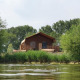 Blick auf eine Lodge am Wasserufer, umgeben von grünen Bäumen und Büschen an einem sonnigen Tag.
