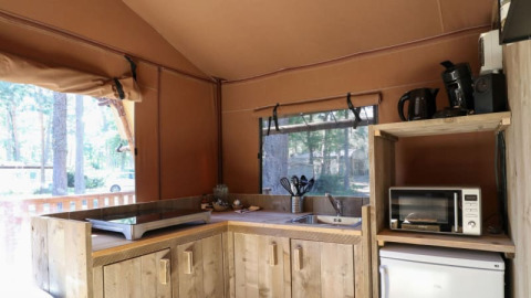 Zona de cocina en una cabaña con placa de cocina, microondas, hervidor, cafetera y armarios de madera.