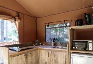 Zona de cocina en una cabaña con placa de cocina, microondas, hervidor, cafetera y armarios de madera.