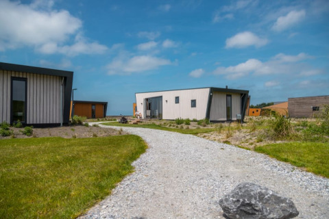 Een kiezelpad loopt naar moderne tiny houses, omringd door gras en een blauwe lucht met wolken.