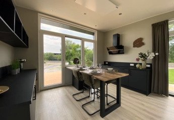 Modern sunny tiny house kitchen with large windows, black cabinetry, and a dining table set for four people.