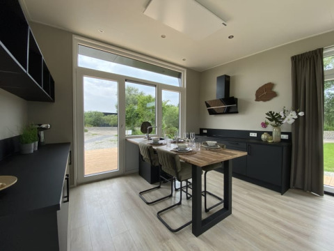 Moderne en lichte tiny house keuken met grote ramen, zwart meubilair en een gedekte tafel voor vier.
