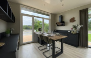 Modern sunny tiny house kitchen with large windows, black cabinetry, and a dining table set for four people.