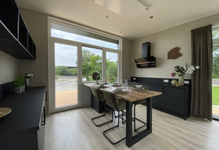 Cucina moderna e luminosa in una tiny house con grandi finestre, mobili neri e tavolo apparecchiato.