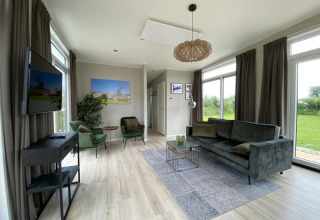 Sala luminosa y moderna de tiny house con sofá verde, sillones, ventanales y vista al jardín.