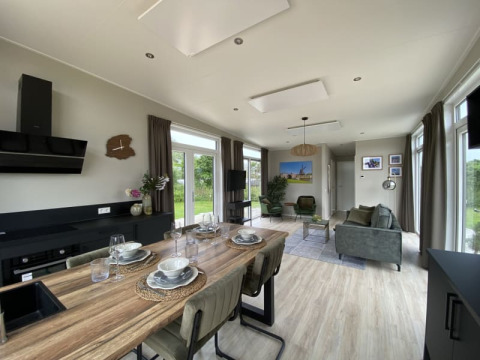 Sala y cocina moderna de tiny house con mesa de comedor, sofás verdes, grandes ventanas y luz natural.