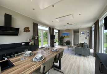 Soggiorno e cucina moderni in una tiny house con tavolo da pranzo, divani verdi e grandi finestre luminose.