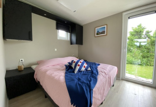 Lichte slaapkamer in een tiny house met dubbel bed, groot raam en zicht op een groene tuin buiten.