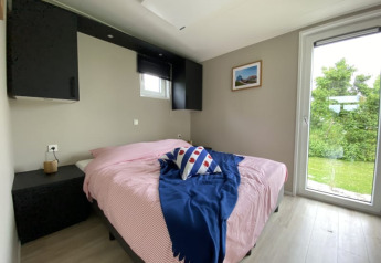 Camera luminosa di una tiny house con letto matrimoniale, grande finestra e vista sul giardino verde.