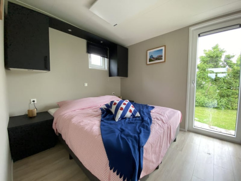 Camera luminosa di una tiny house con letto matrimoniale, grande finestra e vista sul giardino verde.