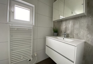 Moderne tiny house badkamer met witte wastafel, spiegelkast, handdoekradiator en klein raam.