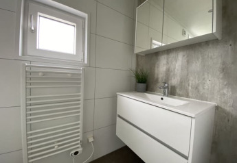 Baño moderno en una tiny house con mueble blanco, espejo, radiador toallero y pequeña ventana.