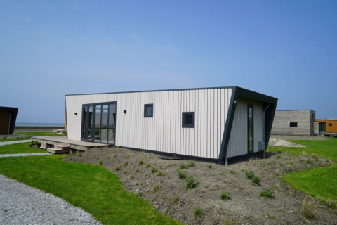 Casa pequeña moderna con revestimiento de madera clara, ventanales y techo angular sobre césped verde.