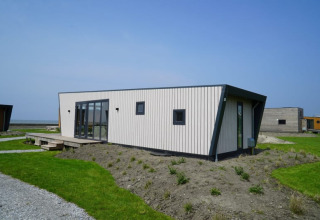 Moderne tiny house met opvallend design en grote ramen, geplaatst op een grasrijk perceel onder blauwe lucht.