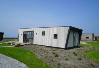 Moderne tiny house med asymmetrisk design, lyse træpaneler og store vinduer, placeret i grønt landskab.