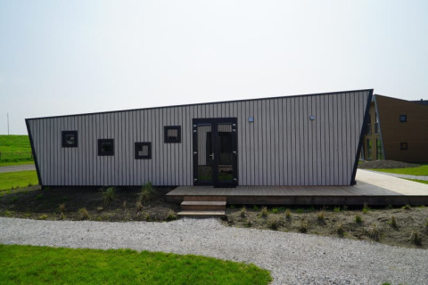 Foto af et moderne tiny house med skråt tag og små kvadratiske vinduer, beliggende i et grønt område.