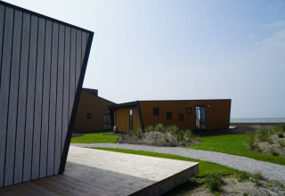 Moderne tiny house met houten gevels en schuine wanden aan de kust, zicht op de zee en graspaden.