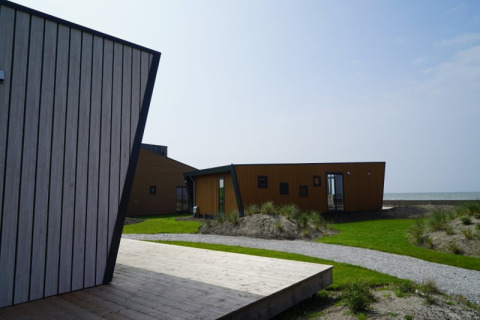Moderne tiny house met houten gevels en schuine wanden aan de kust, zicht op de zee en graspaden.