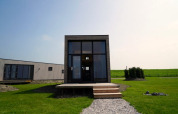 Moderne lodge met grote ramen, houten veranda en groen gazon onder een heldere blauwe lucht.