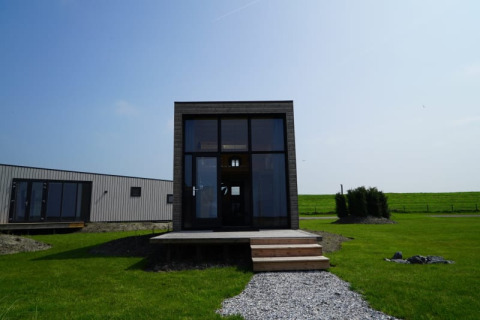Moderne lodge met grote glaspartijen, houten terras en een groen gazon onder een blauwe lucht.