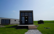 Moderne lodge met grote ramen, houten veranda en groen gazon onder een heldere blauwe lucht.
