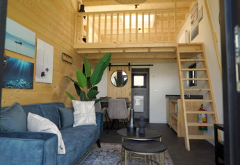 Gemütliche Lodge mit Holzdesign, Schlafempore, blauer Couch, Kunstwerken und kleinem Küchenbereich.