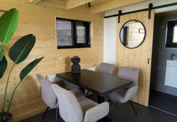 Moderner Essbereich in einer Lodge mit Holzverkleidung, schwarzen Fenstern, beigen Stühlen und Pflanze.