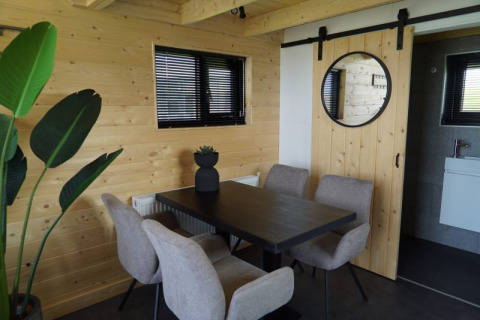 Comedor moderno de lodge con paredes de madera clara, ventanas negras, silla beige, mesa y planta verde.