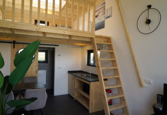 Moderne Lodge mit Hochbett, Holztreppe, Küchenzeile und Essbereich unter natürlichem Licht.