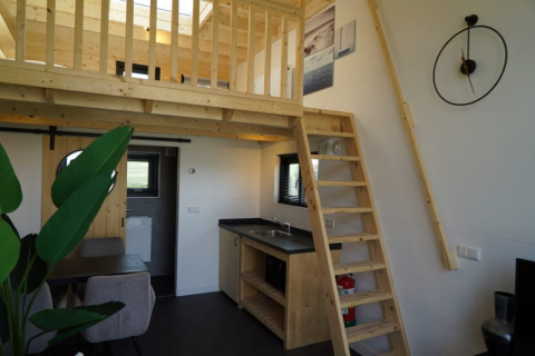 Modern lodge-interieur met houten tussenverdieping, ladder, kleine keuken en gezellige eetruimte.