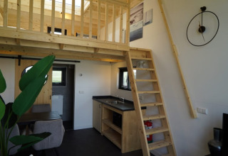 Modern lodge-interieur met houten tussenverdieping, ladder, kleine keuken en gezellige eetruimte.