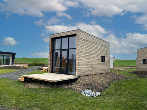 Lodges modernes en bois avec grandes fenêtres, situés dans une zone verte sous un ciel bleu légèrement nuageux.
