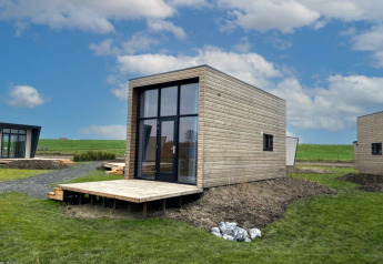 Moderne Lodge-Hütten mit großen Fenstern und Holzverkleidung in einer grünen Landschaft bei blauem Himmel.