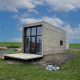 Moderne lodgehytter med store vinduer og træbeklædning, placeret i et grønt område under blå himmel.