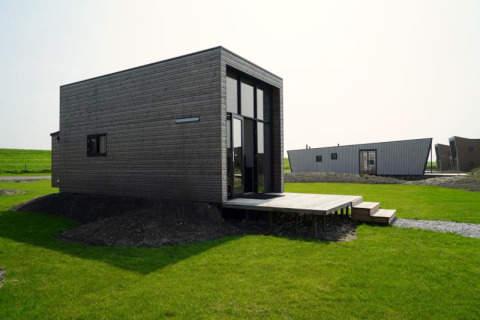 Lodge moderne en bois foncé avec de grandes fenêtres, situé sur une pelouse verte sous un ciel dégagé.