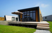 Moderne lodge met houten terras, tuinmeubilair en parasol, gelegen op gras en omringd door andere lodges.