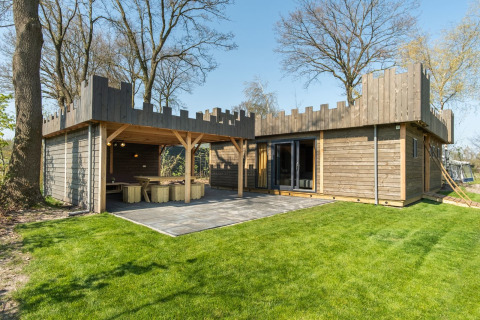 Træhytte inspireret af et slot med tårnvægge, grøn græsplæne og udendørs spiseområde i Holland.
