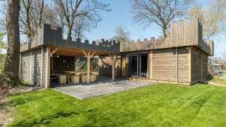 Cabaña tipo castillo de madera con muros almenados, césped verde y terraza en los Países Bajos.