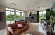 Licht, modern lodge-interieur met open keuken, eethoek en woonkamer met uitzicht op groene natuur.