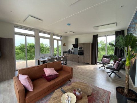 Intérieur de lodge moderne et lumineux avec cuisine ouverte, salon et grandes fenêtres sur la verdure.