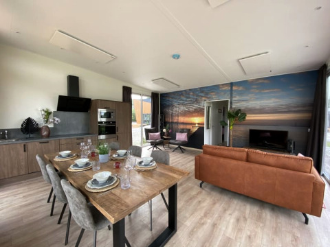 Intérieur de lodge moderne avec cuisine ouverte, table à manger, salon et fresque murale de coucher de soleil.
