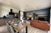 Moderne lodge met open keuken, eettafel, zithoek en een groot muurschilderij van een zonsondergang.