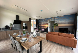 Intérieur de lodge moderne avec cuisine ouverte, table à manger, salon et fresque murale de coucher de soleil.