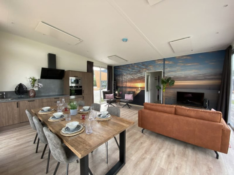 Modern lodge-interieur met open keuken, eetruimte, zithoek en een groot muurkunstwerk van een zonsondergang.
