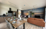 Intérieur de lodge moderne avec cuisine ouverte, table à manger, salon et fresque murale de coucher de soleil.