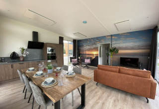 Modern lodge-interieur met open keuken, eetruimte, zithoek en een groot muurkunstwerk van een zonsondergang.